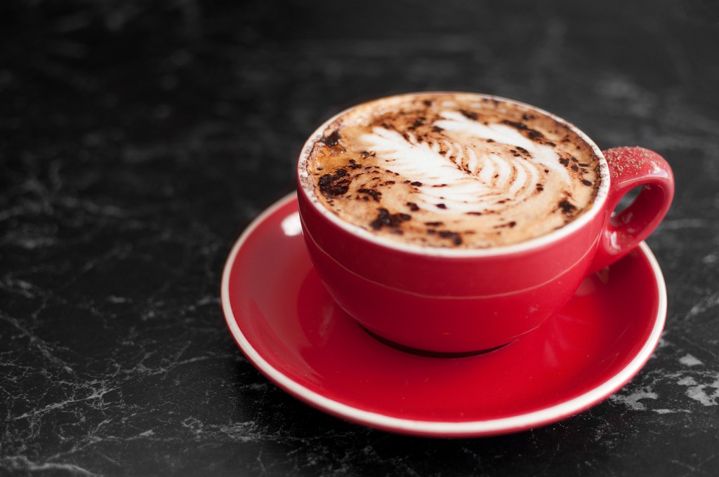 A red cup and saucer holds a cappuccino coffee with a sprinkling of chocolate